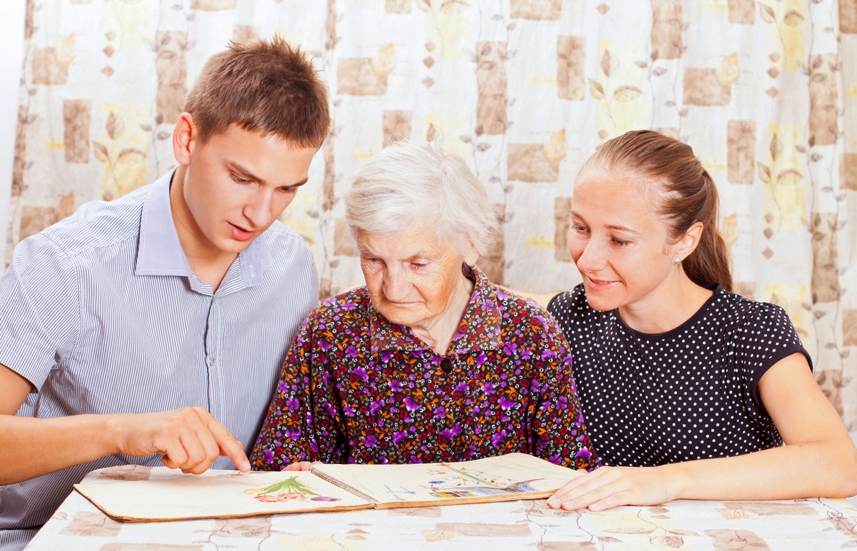 young caregivers helping an elderly woman to read